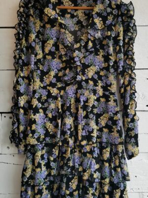 Vestido estampado negro con flores amarillas y moradas. Manga larga. Olanes en manga, escote y falda.