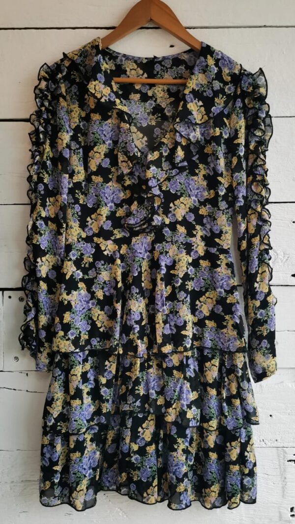 Vestido estampado negro con flores amarillas y moradas. Manga larga. Olanes en manga, escote y falda.